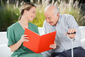 Smiling female nurse looking at senior man while reading book in nursing home